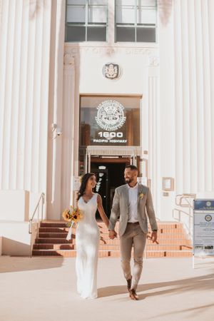 Wedding couple strolling and laughing outside a grand building with white pillars.