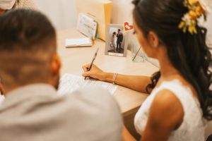 Couple signing wedding documents together at a desk with framed photo.
