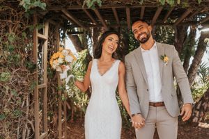 Happy wedding couple laughing together under rustic pergola with sunflower bouquet.