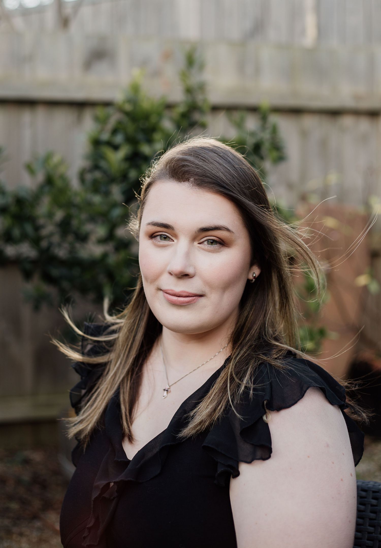 Outdoor portrait with wind-swept hair against wooden fence background.