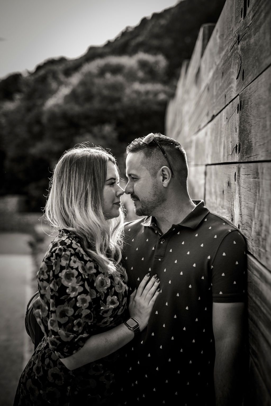 An intimate black and white portrait of a couple sharing a tender moment against a wooden wall.