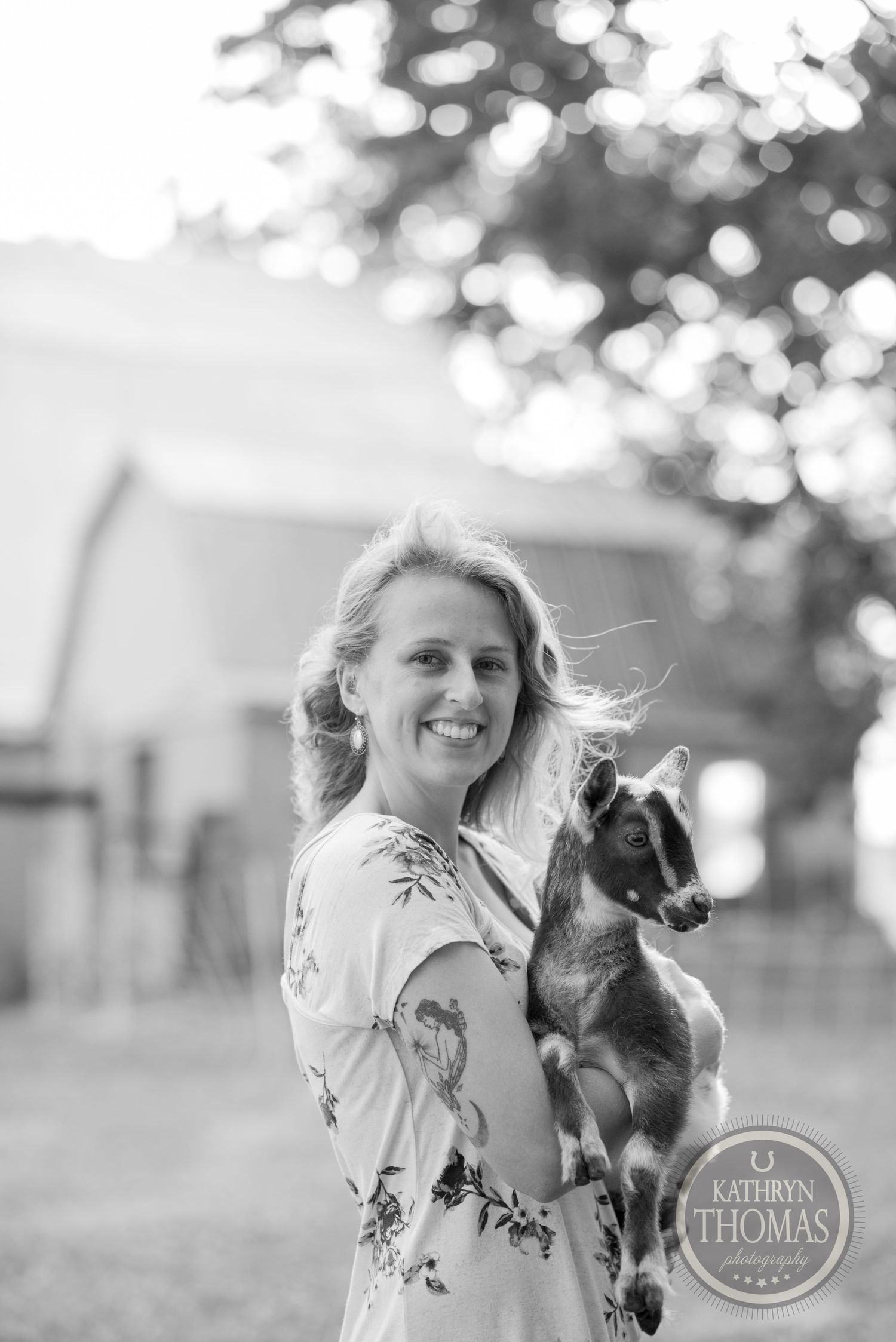 A person in floral dress holds a small cat outdoors in black and white photography.