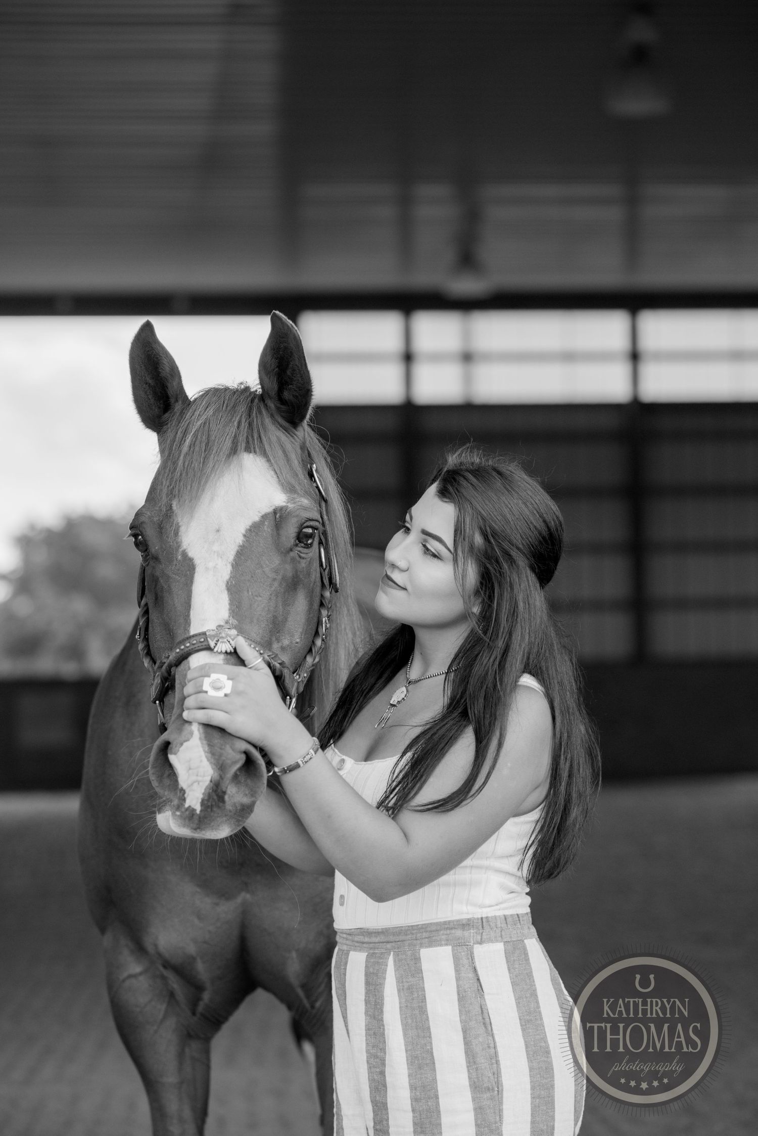 A monochrome portrait of a horse receiving gentle attention in a stable.