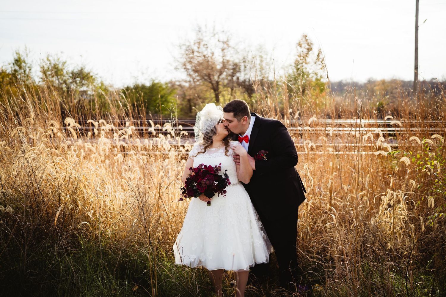 Wedding couple embracing in tall autumn grass during golden hour.