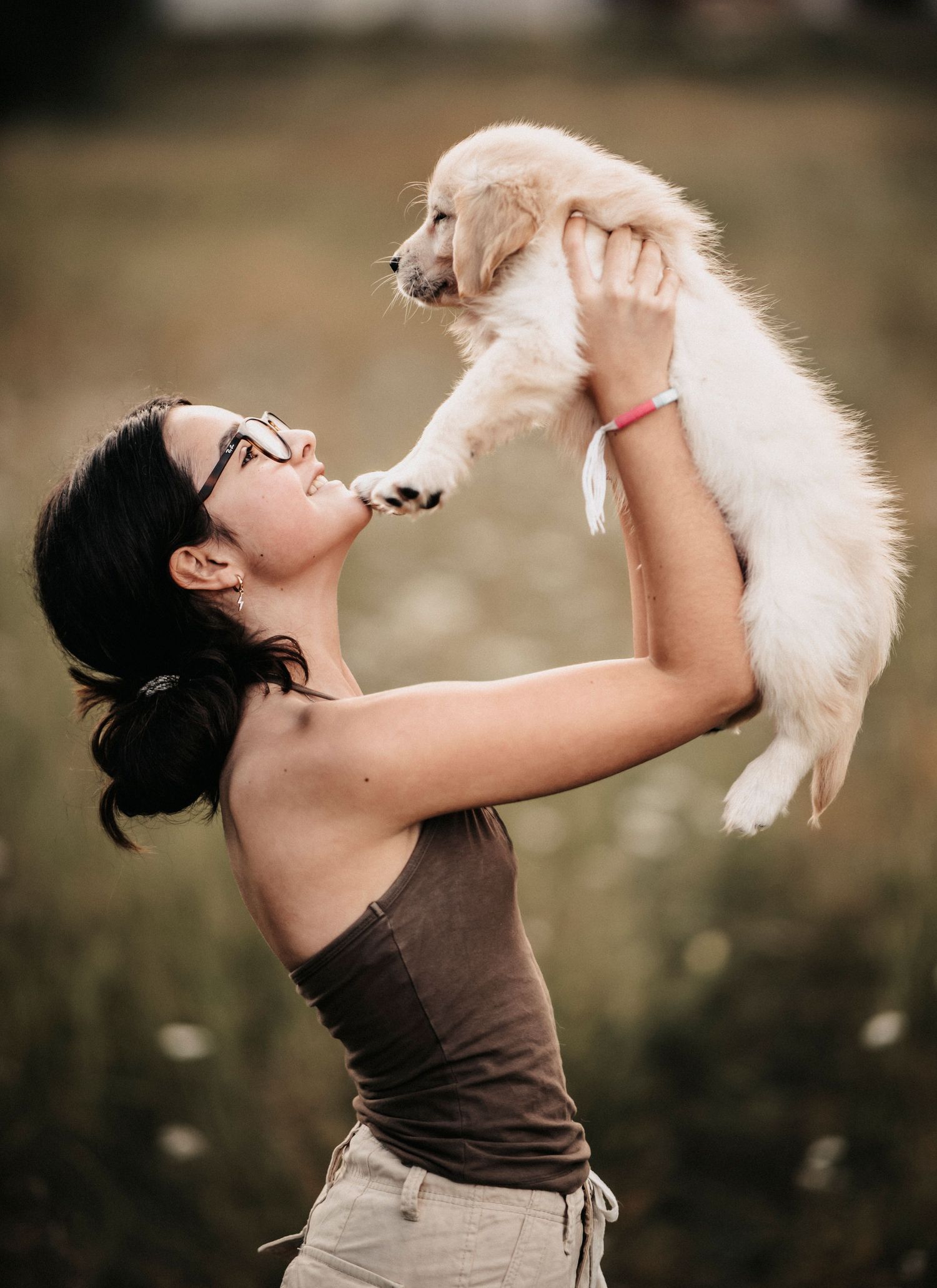 A joyful moment captured between a person and their fluffy white puppy held up against a blurred outdoor background.
