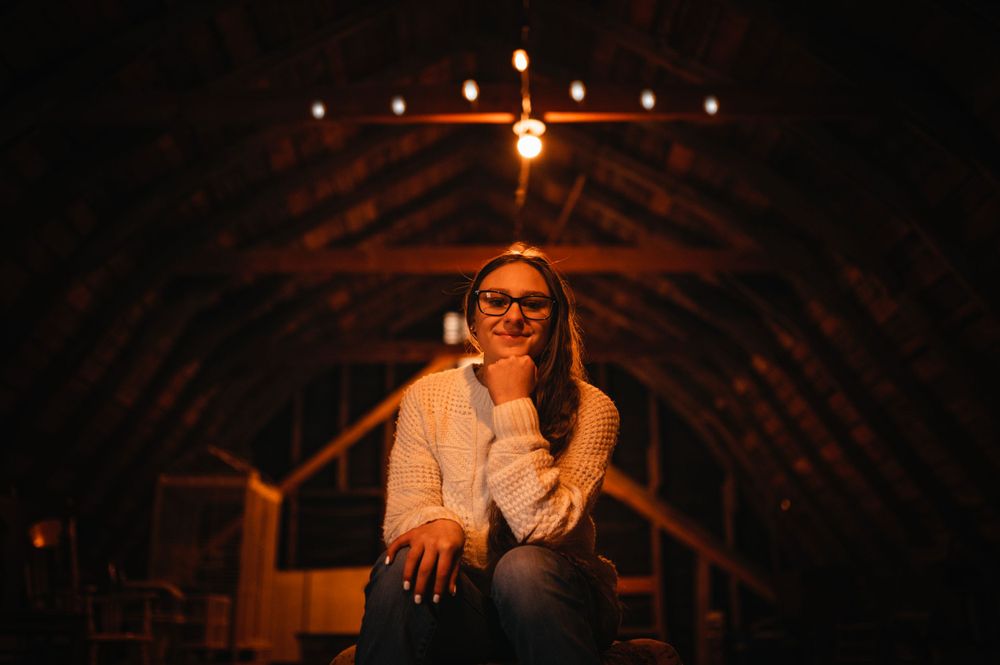 Senior girl in white sweater in dark room for photosession in Cook, MN.