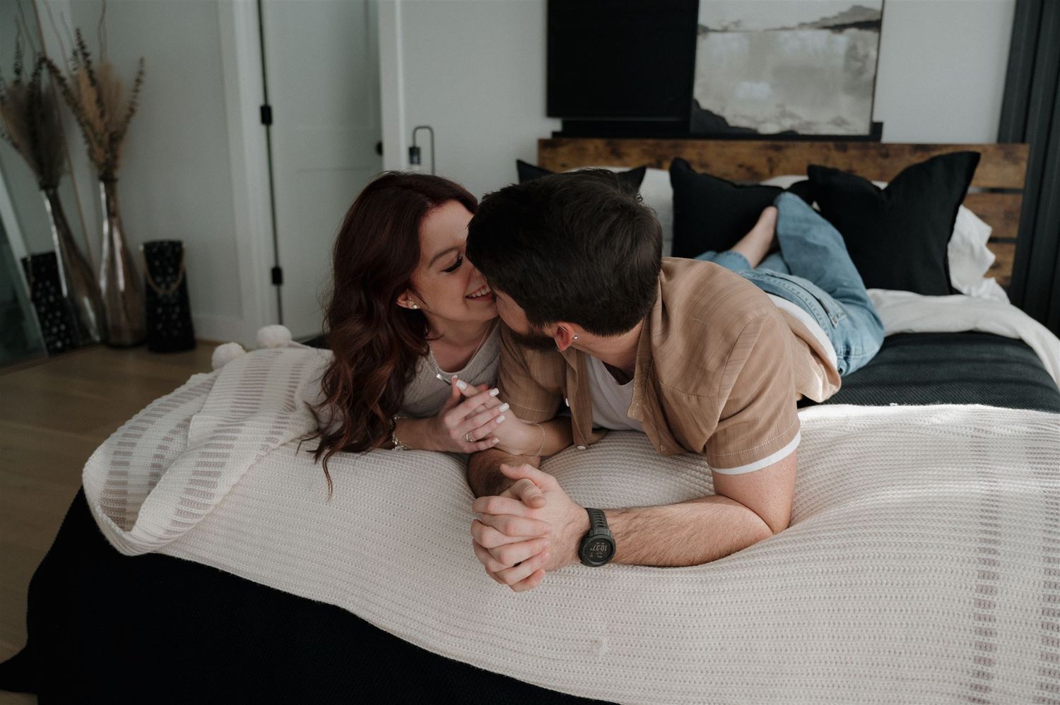 Couple sharing an intimate moment while holding hands on white bedding.