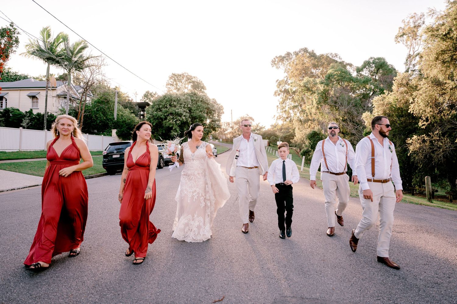 Wedding party walking down street with bridesmaids in red dresses and groomsmen in white.