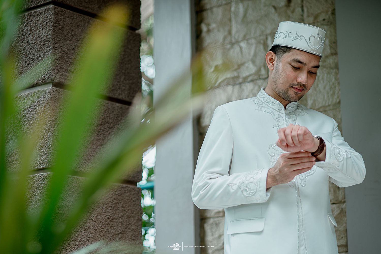 A groom in traditional white attire clasps his hands in prayer or reflection.