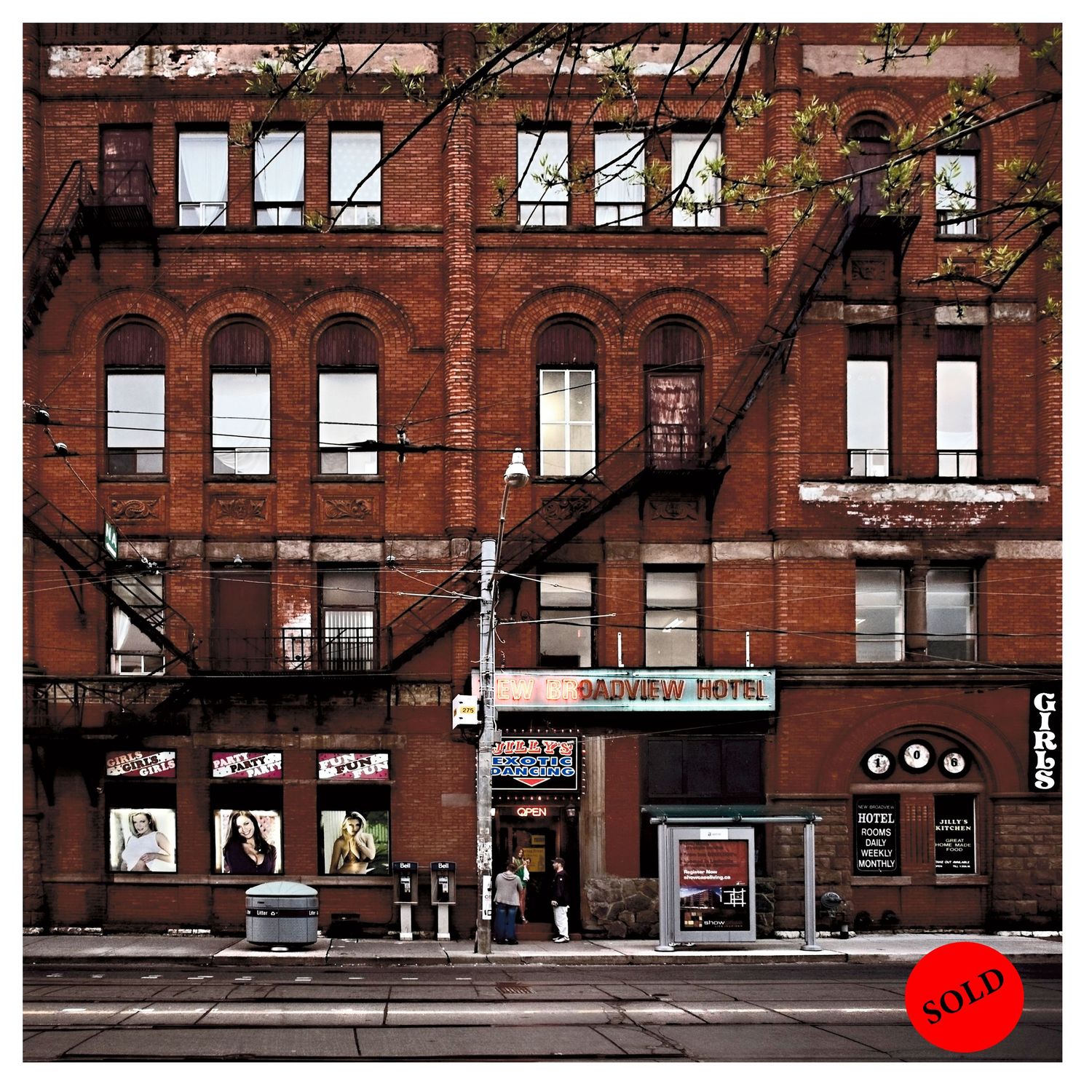 Red brick apartment building facade with fire escapes and storefronts in urban setting.