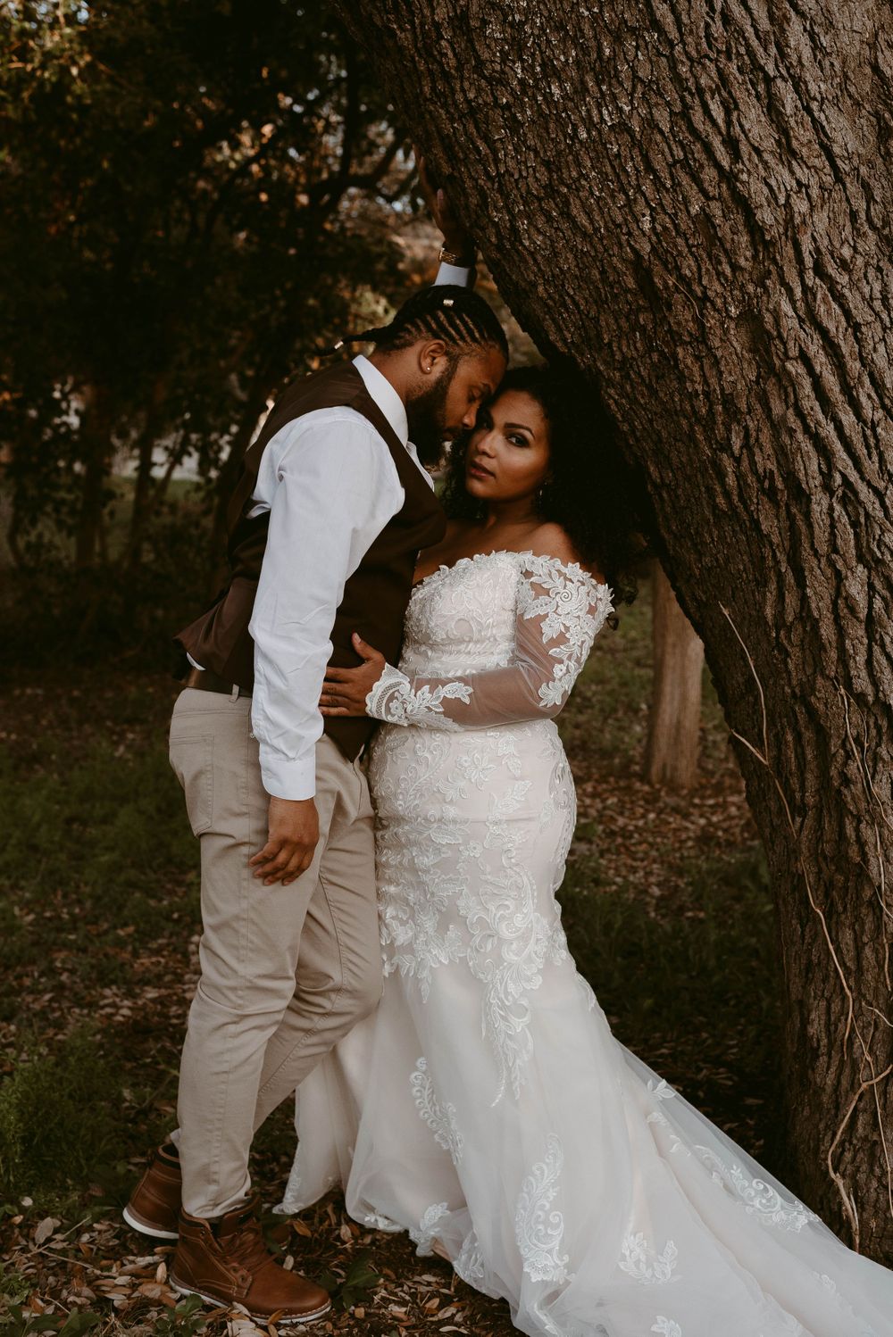Intimate wedding portrait of couple sharing tender moment against large tree trunk.