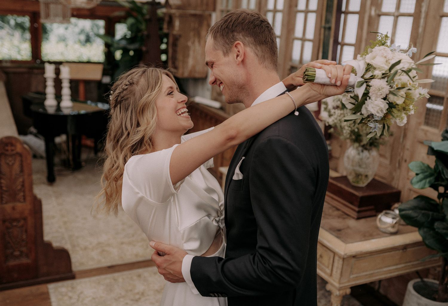 Romantic wedding couple embracing while holding a delicate white floral bouquet.