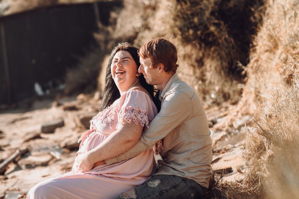 Joyful maternity moment captured of couple laughing together on rocky terrain.