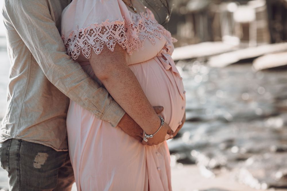 Close-up of embracing couple's hands on pregnant belly during outdoor photoshoot.