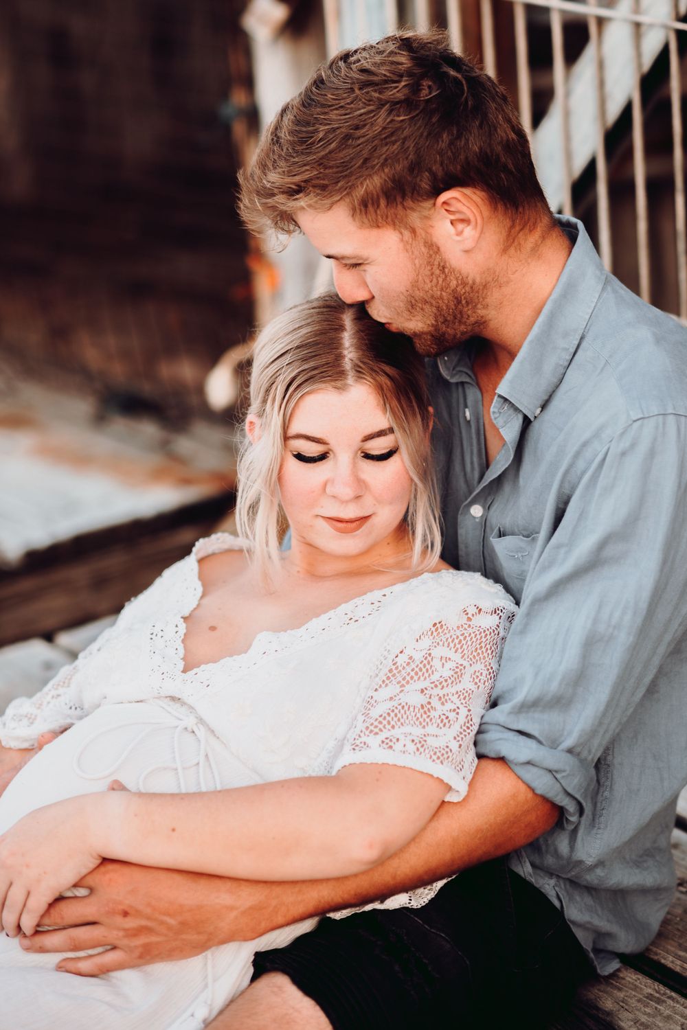 Intimate moment between couple during maternity session on wooden deck.