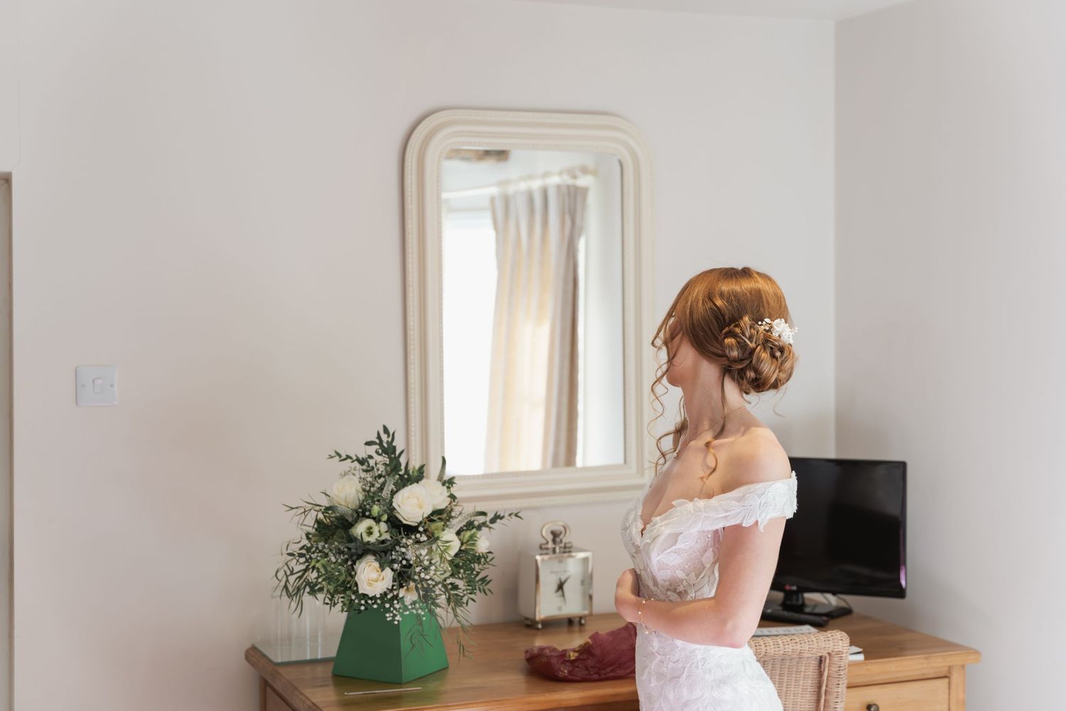 White dress and elegant decor reflected in mirror during wedding preparations.