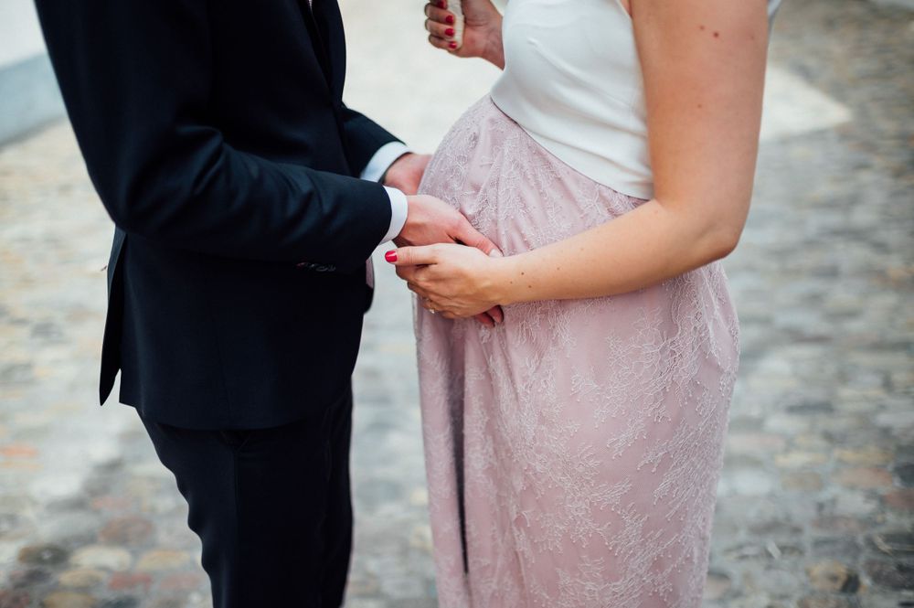Close-up view of formal attire and clasped hands against a cobblestone street background.