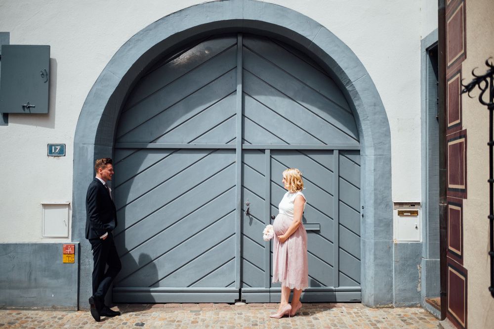A couple standing on opposite sides of a large grey arched door in an urban setting.