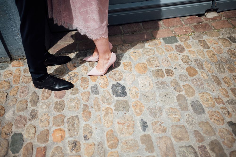 Formal black shoes and pink heels on historic cobblestone pavement.
