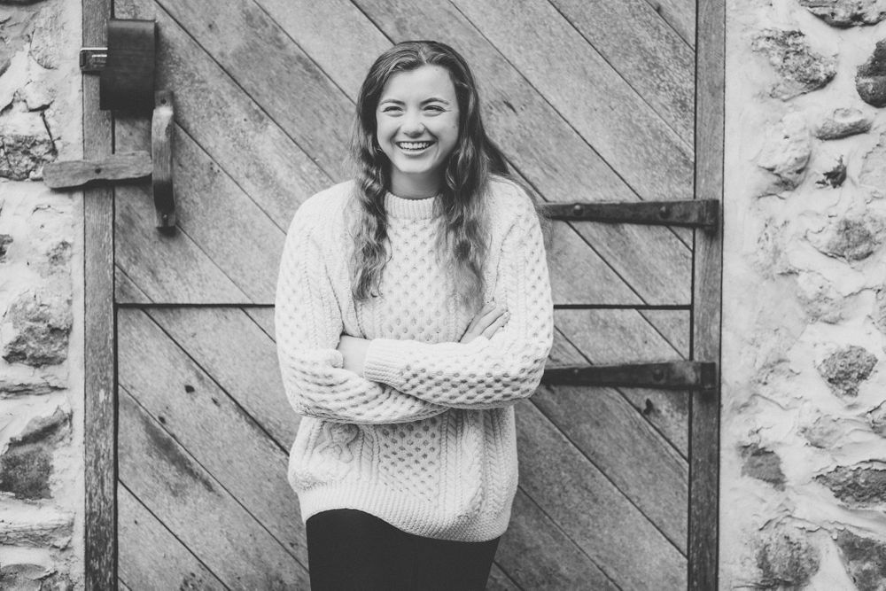 Black and white portrait against a rustic wood and stone wall background.