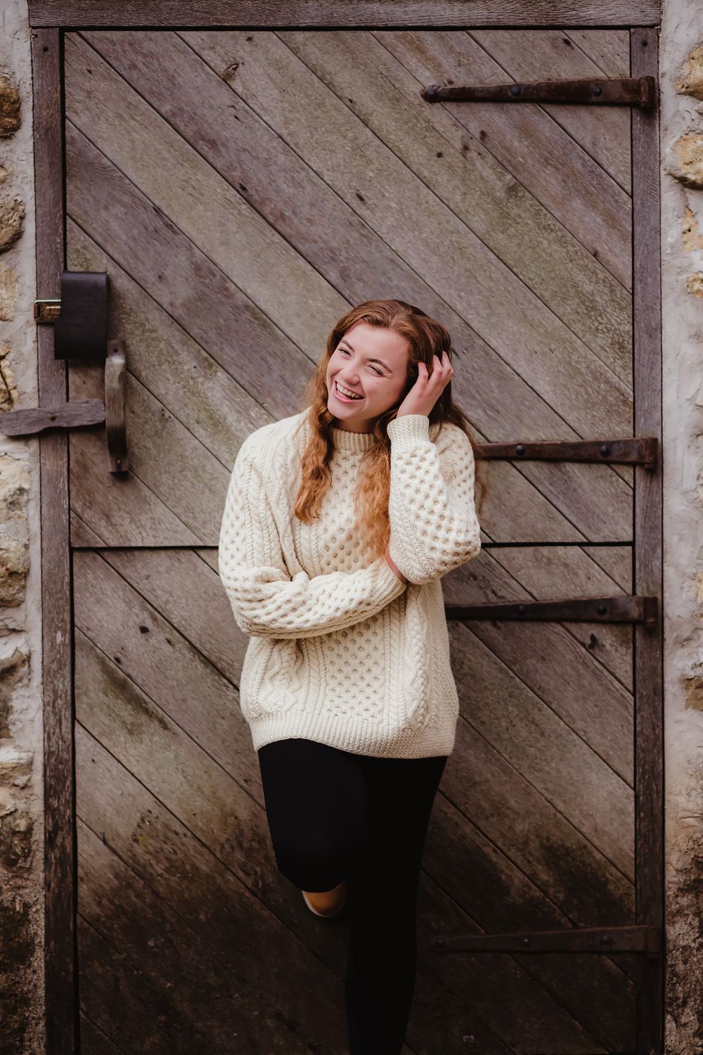 Casual portrait against a weathered wooden barn door wearing a cozy knit sweater.