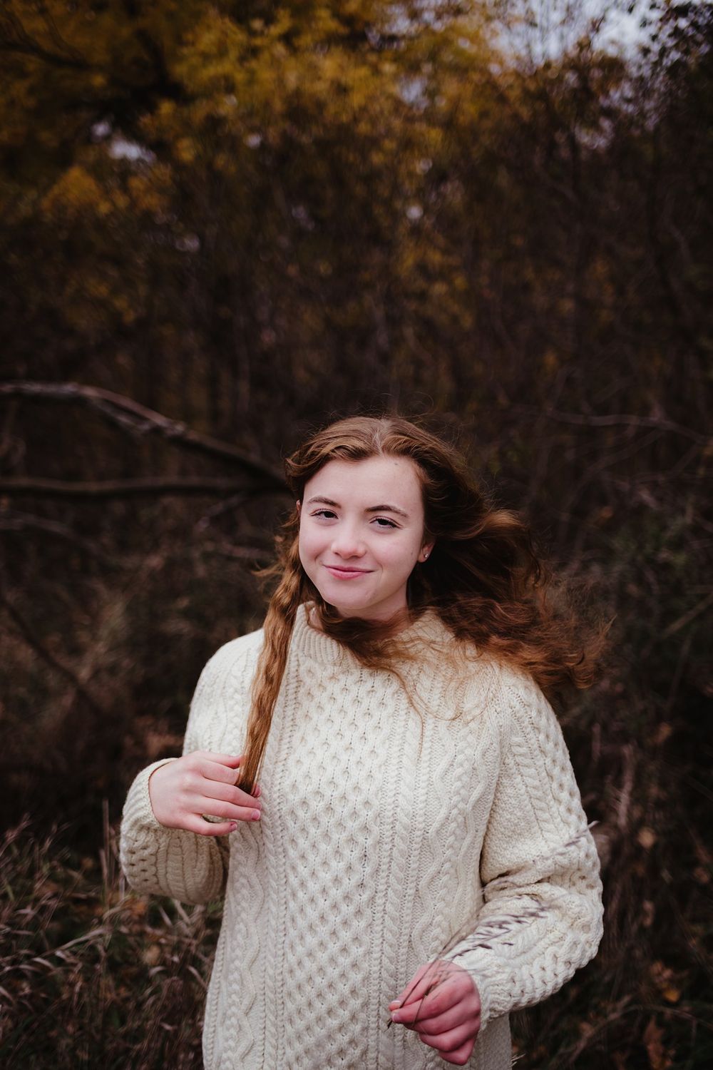 Person wearing cream cable knit sweater standing outdoors during fall season.