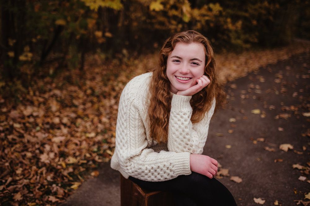 Person in cable knit sweater sitting casually on autumn path.