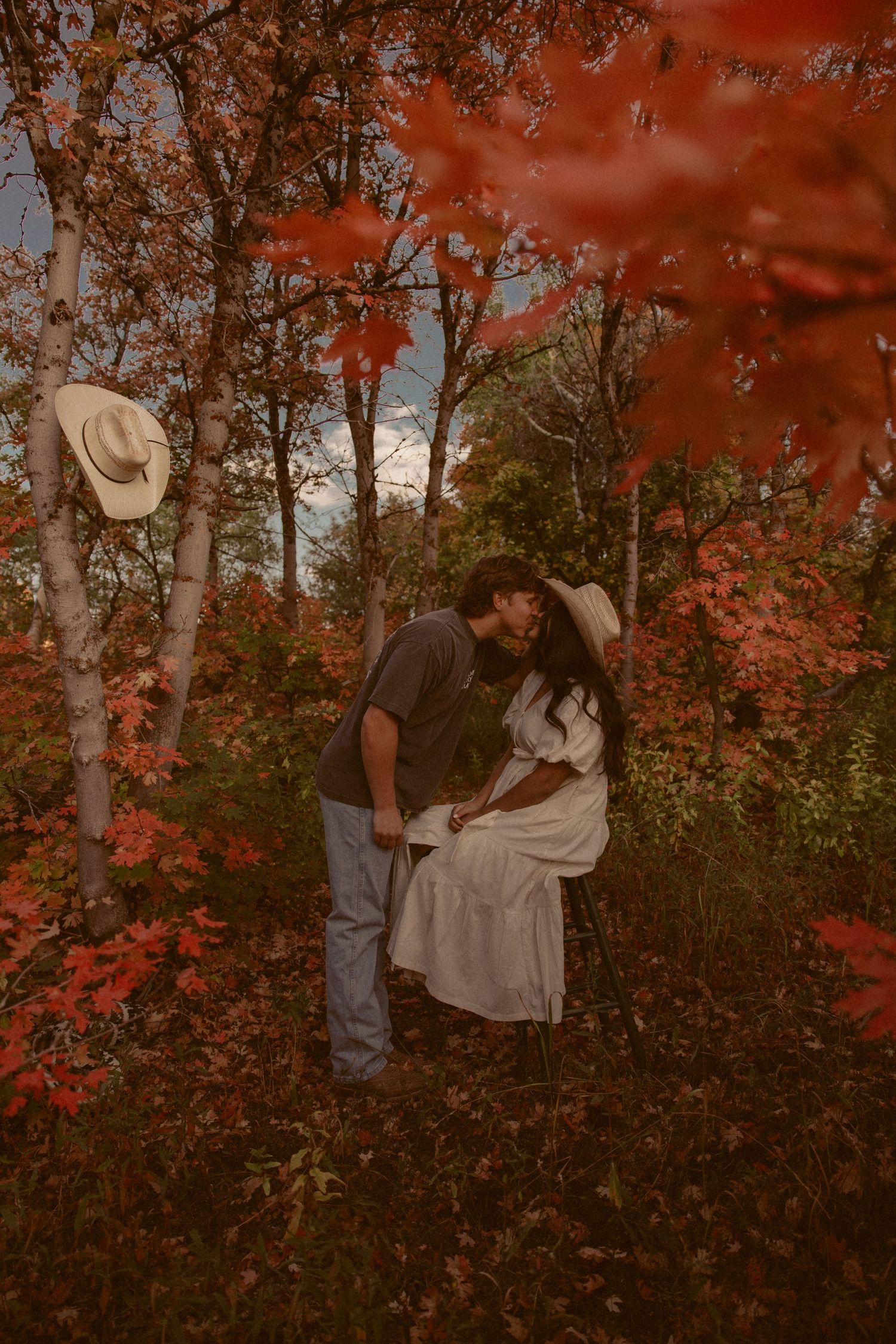 Romantic autumn scene with couple embracing among red maple leaves and trees.