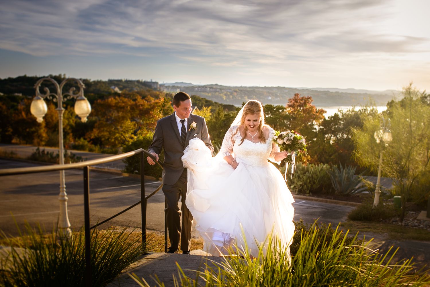 Bride and groom walking on outdoor terrace at sunset with scenic mountain view.