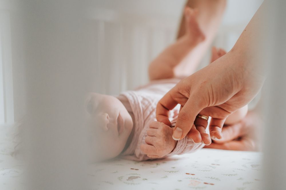 mama trzymająca za rączkę noworodka leżącego w łóżeczku - sesja noworodkowa domowa Kraków