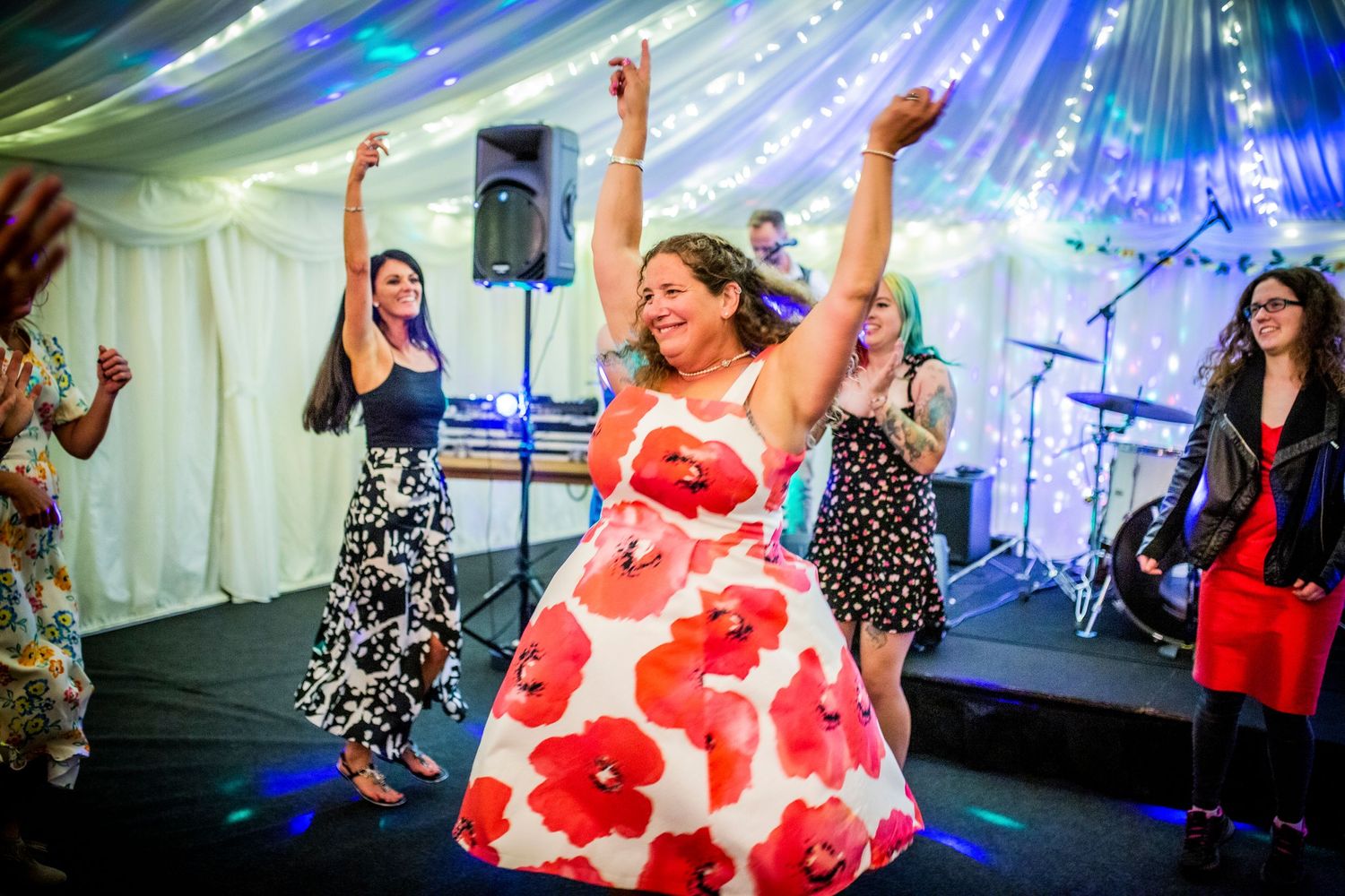 Wedding guests dancing and celebrating under dramatic blue tent lighting.