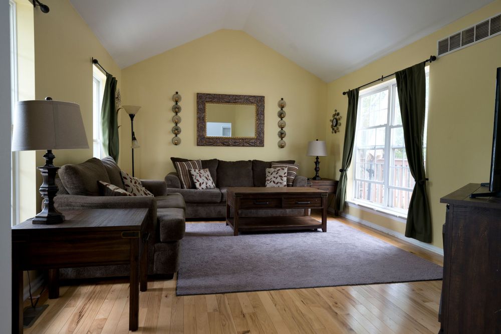 Cozy living room with brown sectional sofa, dark curtains, and hardwood floors beneath a plush area rug.