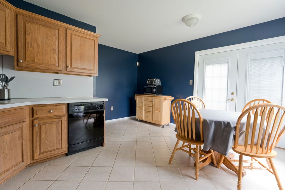 Modern kitchen with oak cabinets and navy blue walls featuring a round dining table with wooden chairs.