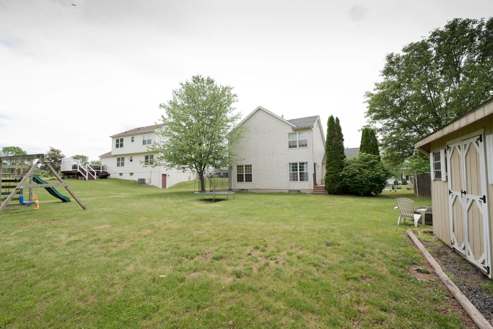 Large backyard with playground equipment and storage shed behind a two-story suburban home.