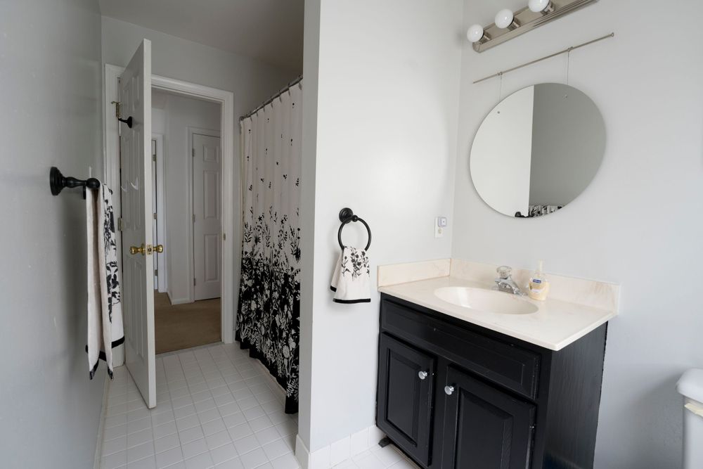 Clean white bathroom with black vanity cabinet, circular mirror, and decorative wall accents.