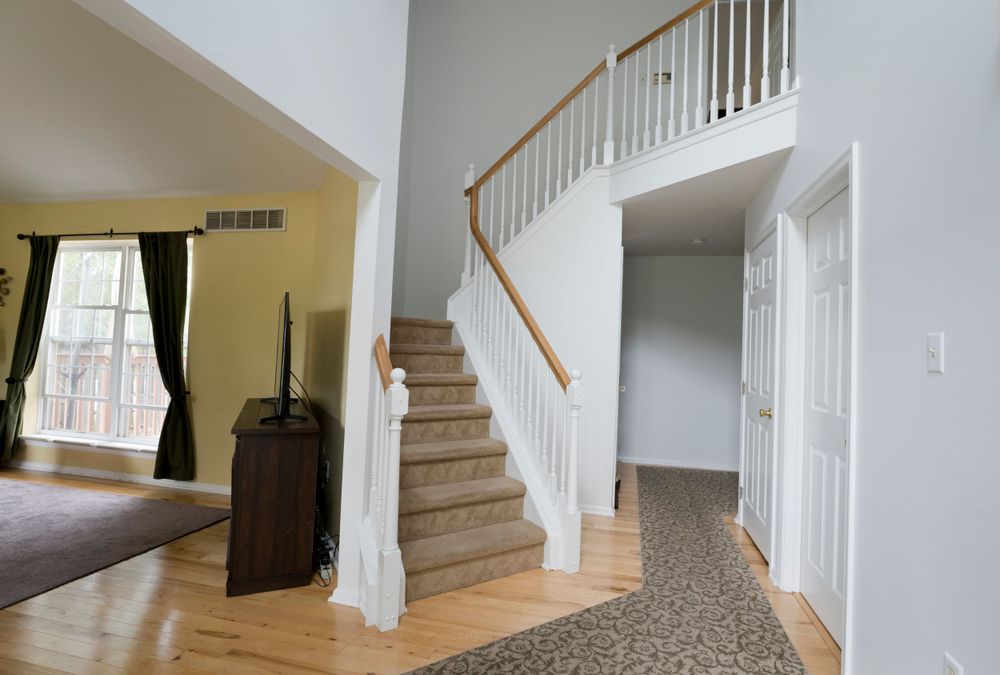 Modern home entrance with curved wooden staircase, hardwood floors and dark curtains in living room.