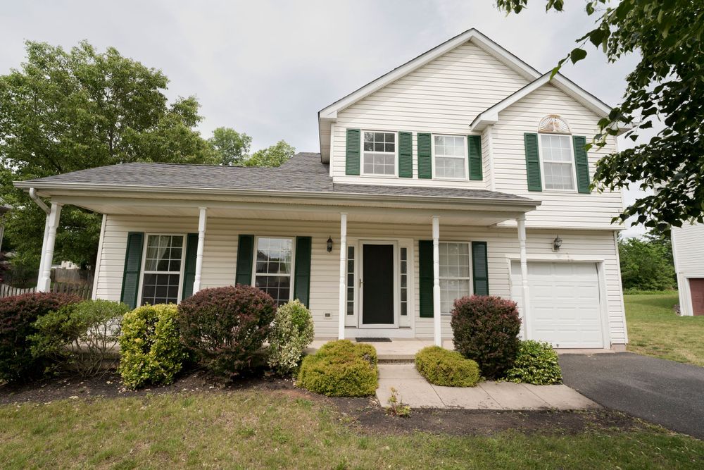 Traditional two-story white house with green shutters, covered porch, and attached garage.