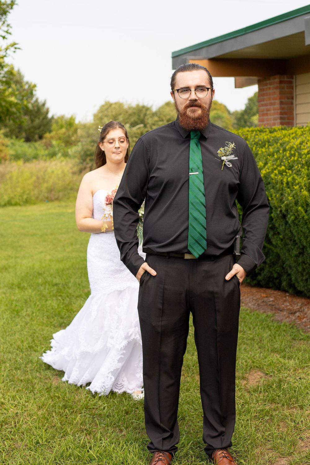 A wedding photo showing a couple in formal attire posing near a building exterior.