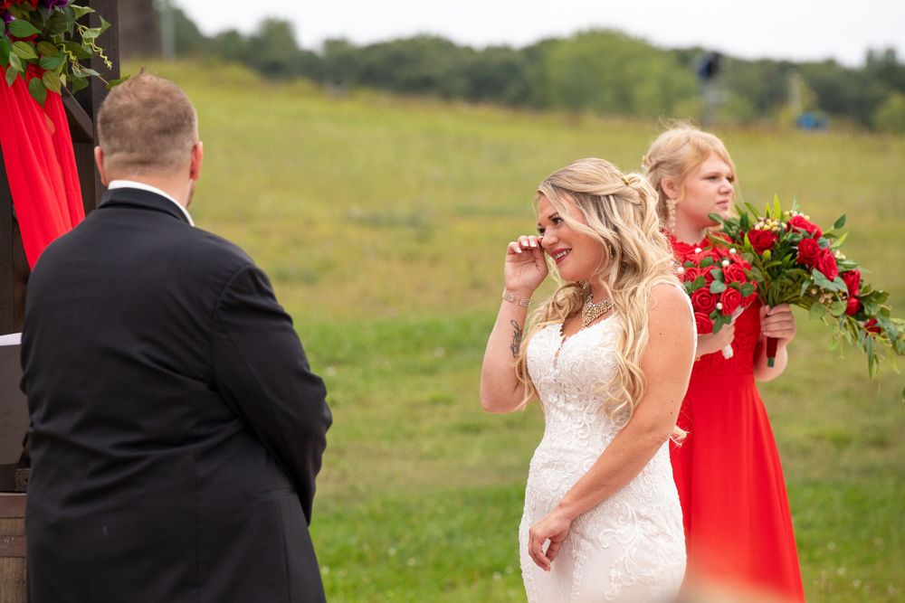 An emotional moment during an outdoor wedding ceremony with guests in the background.