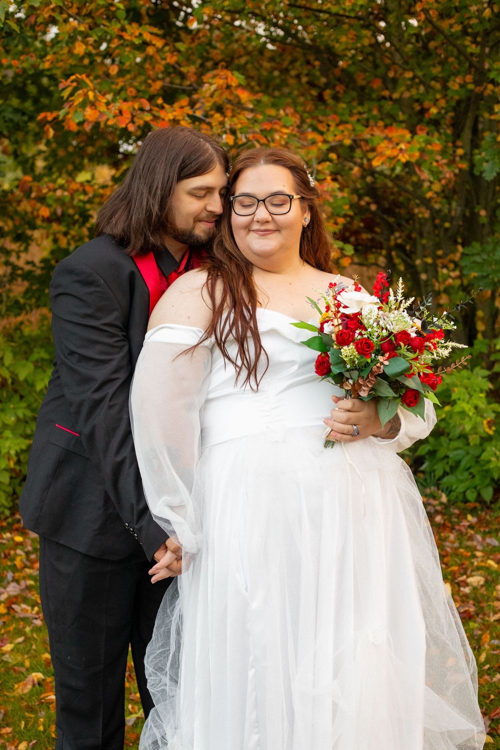 A couple shares an intimate moment in their wedding attire against autumn foliage.
