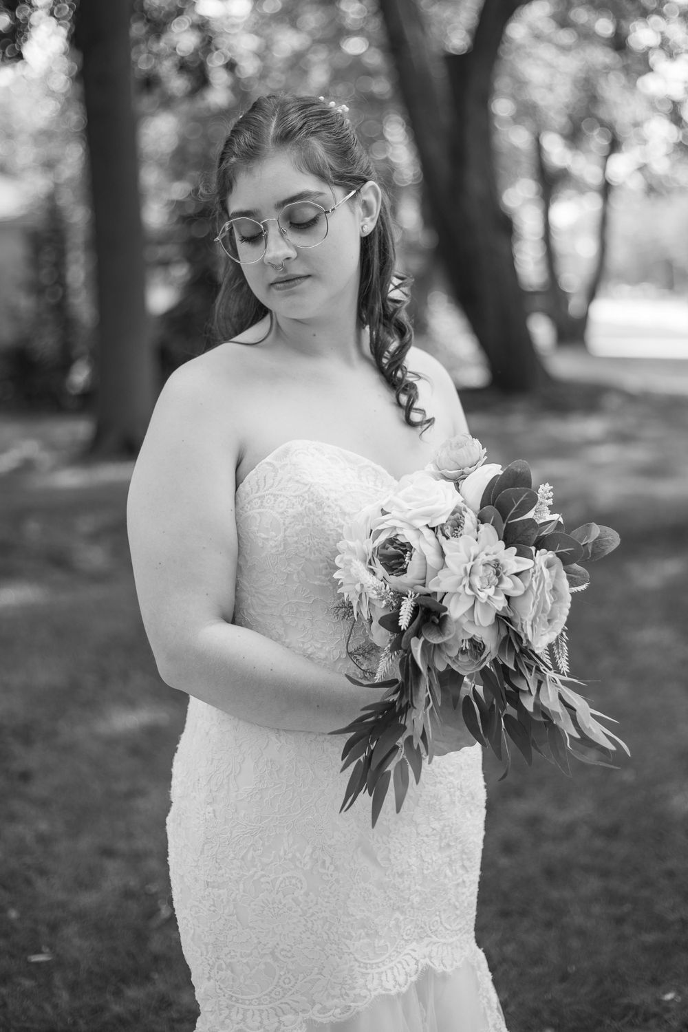 A black and white portrait of a bride holding a floral bouquet in a garden setting.