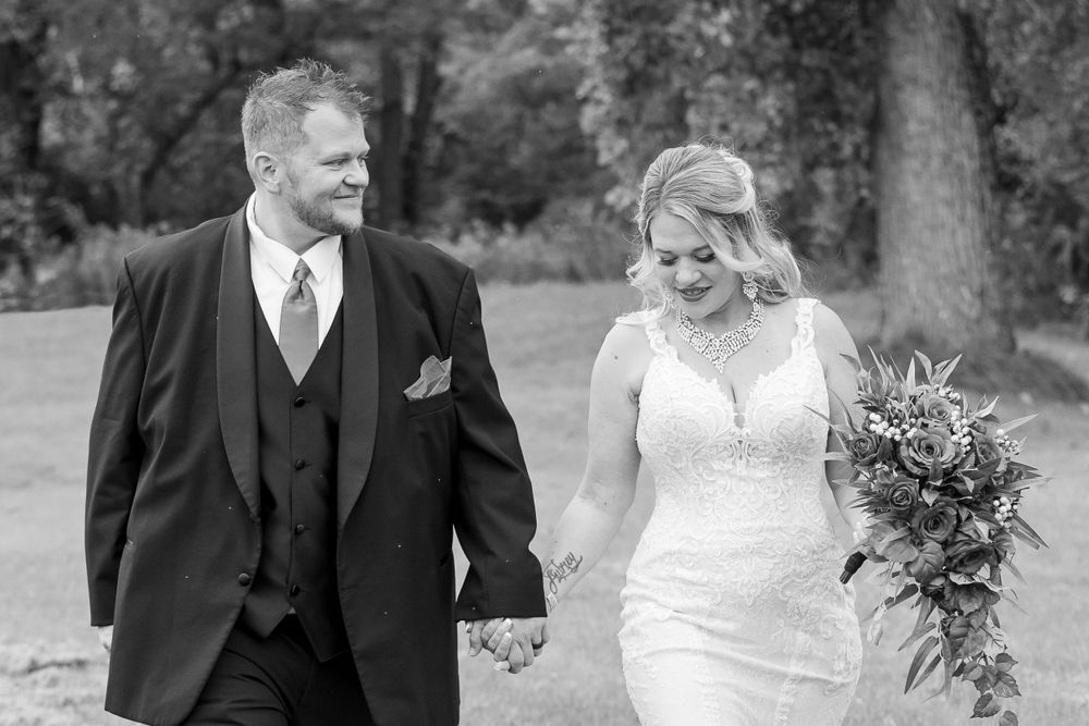 A romantic black and white wedding photo of a couple walking together through a garden setting.