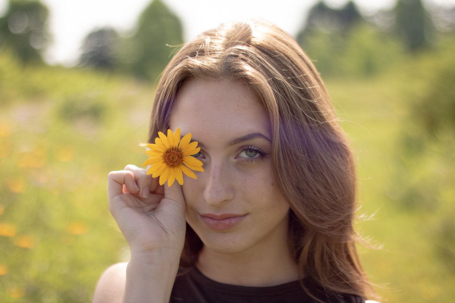 Creative portrait with bright yellow sunflower against natural outdoor backdrop.