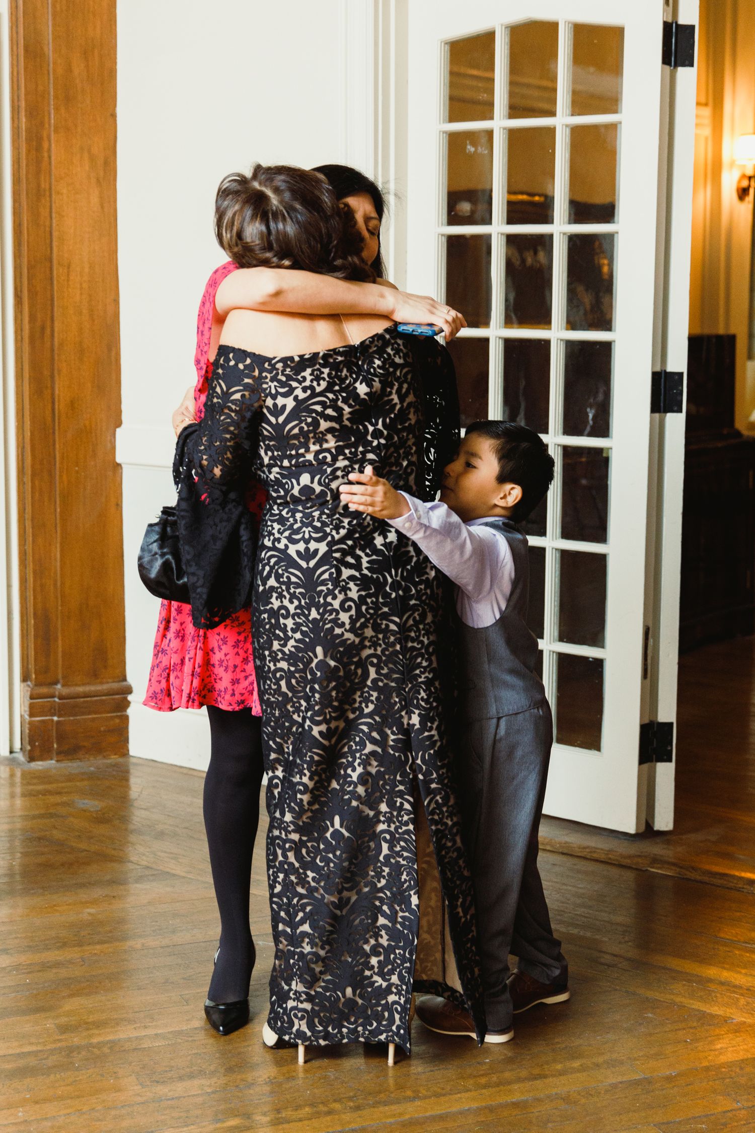 People dancing and hugging in formal attire at an indoor wedding reception.