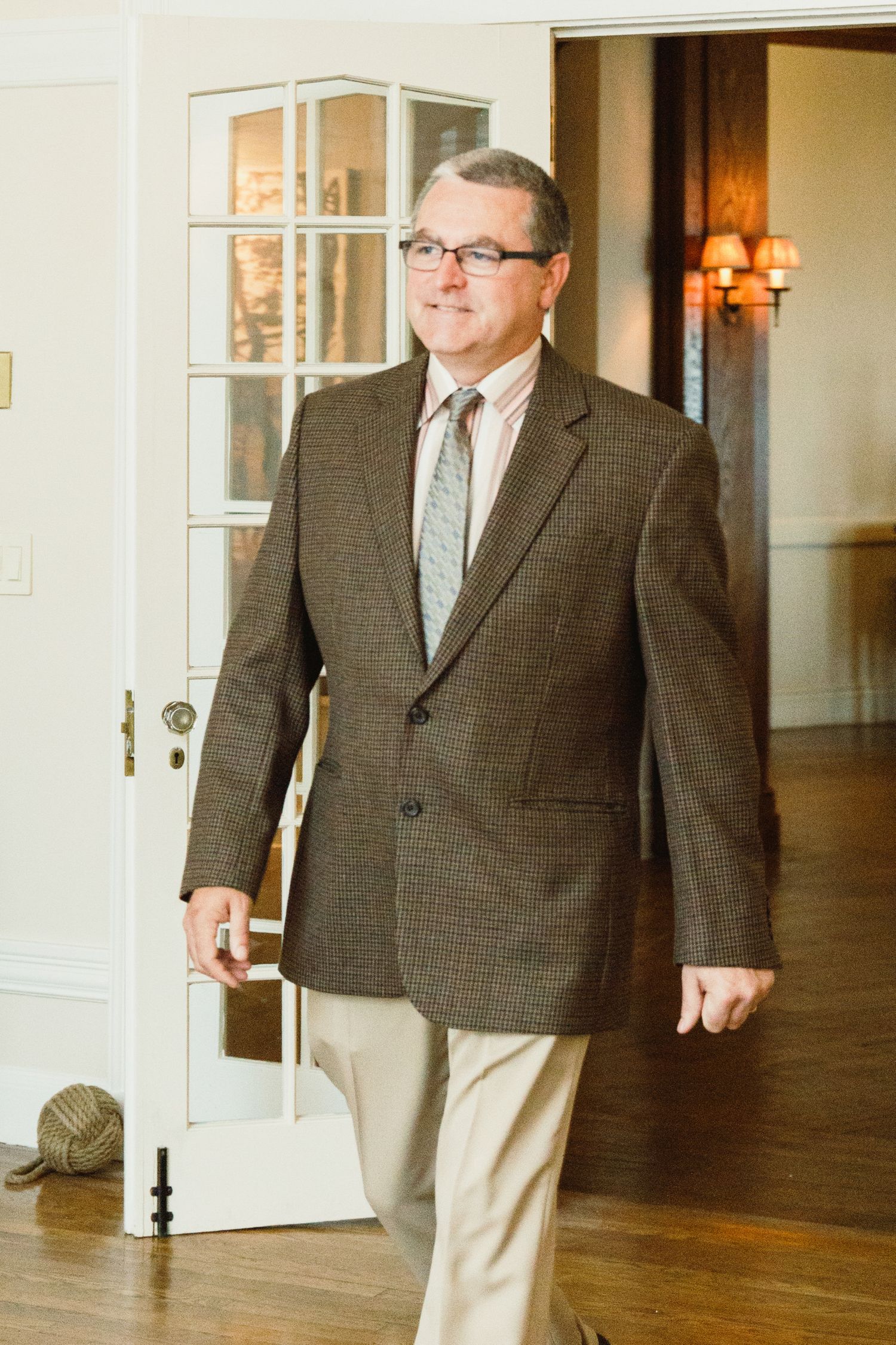 A person wearing a brown plaid blazer and khaki pants walks through an elegant indoor venue.