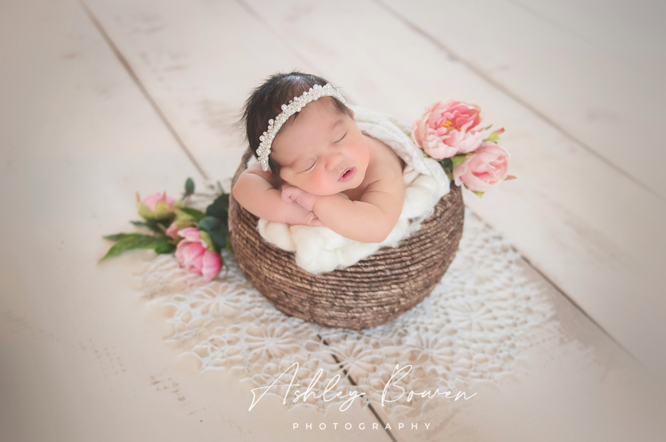 Smiling newborn baby girl in a woven basket with pink roses and a lace headband.