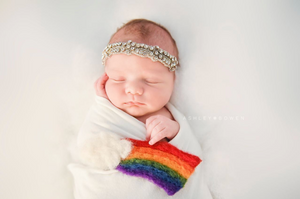 Sleeping newborn wrapped in white swaddle with rainbow knit detail and crystal headband.