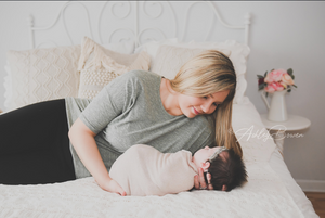 Mother lovingly gazing at swaddled newborn baby on white bed during photoshoot.