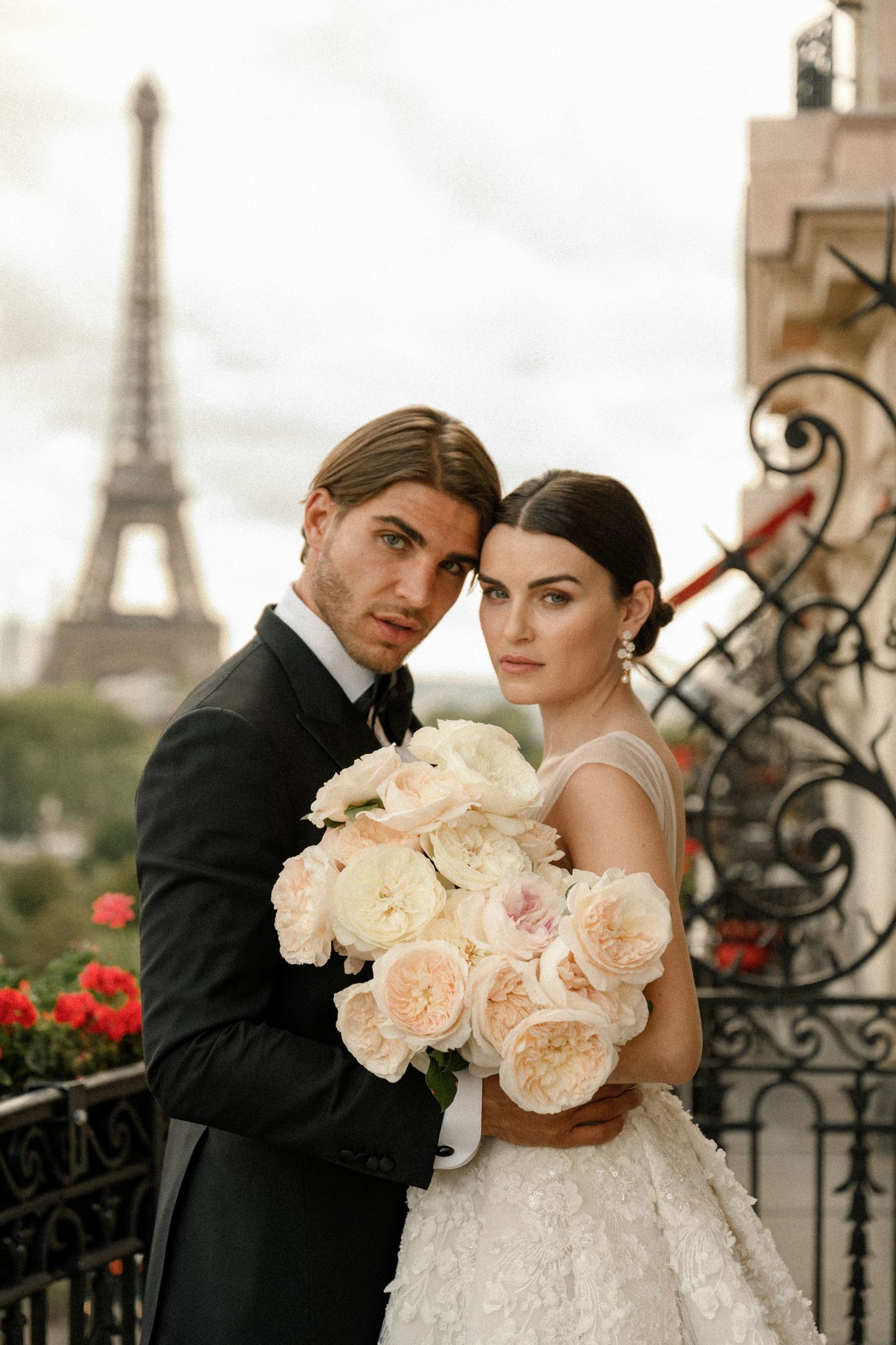 Romantic wedding portrait on Paris balcony with Eiffel Tower and pink roses in background.