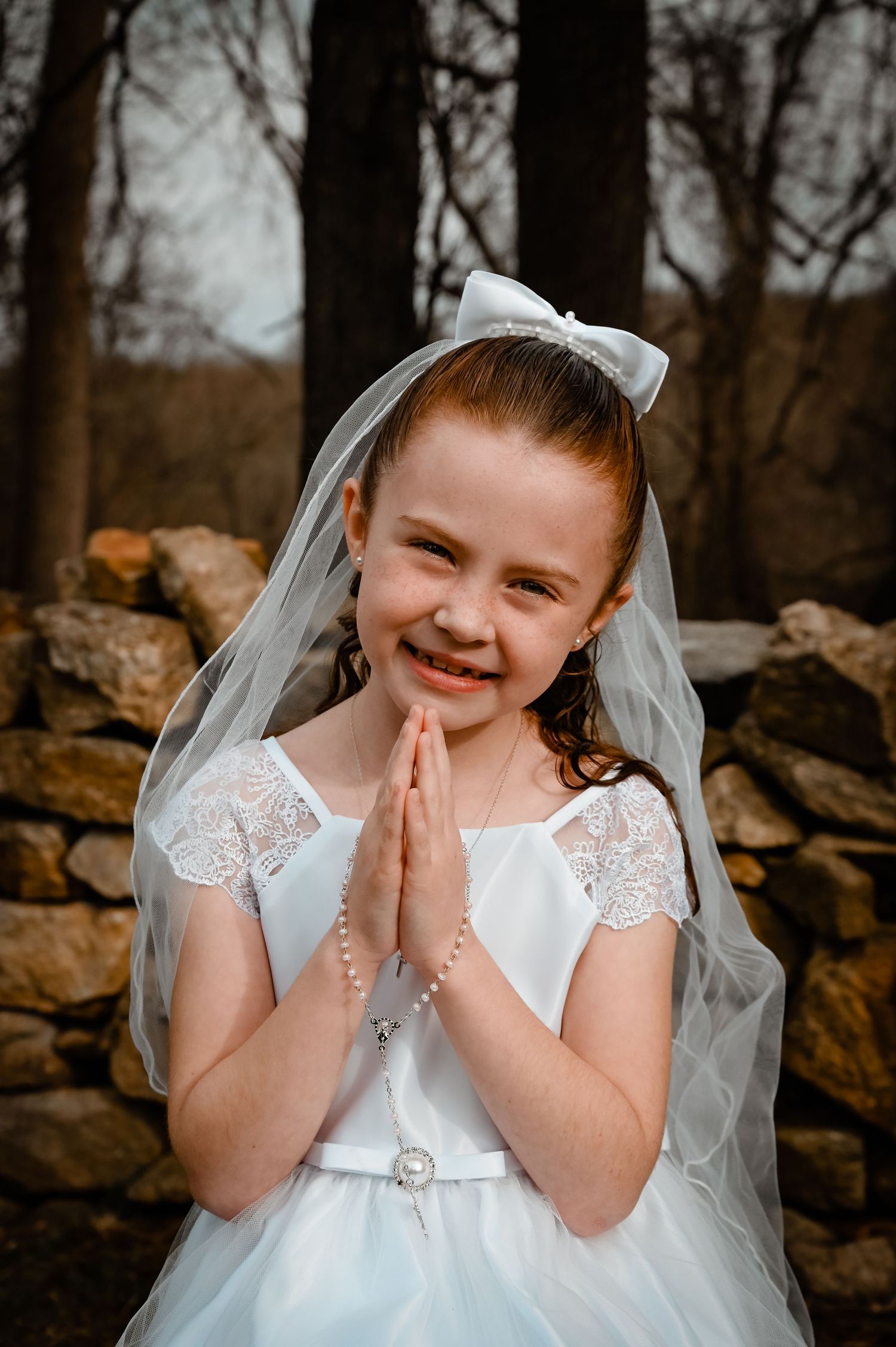 A young child in a white communion dress and veil expresses pure joy and excitement.